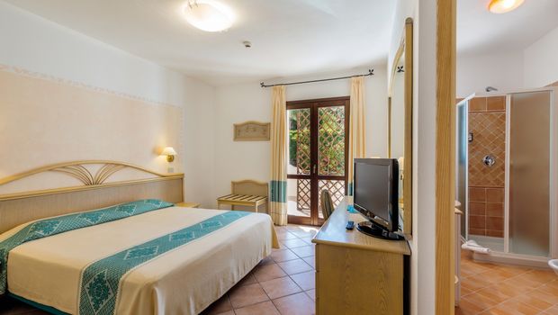 Helles und freundlich eingerichtetes Hotelzimmer mit Doppelbett, Schreibtisch, Fernseher und Zugang zum Balkon – Blick ins angrenzende Bad mit Dusche.
