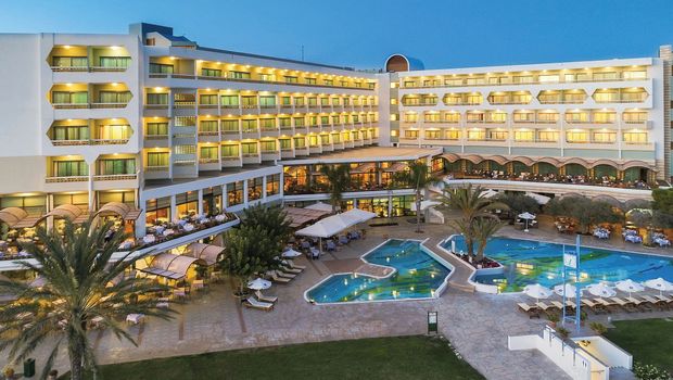 Abendaufnahme eines großen Hotels mit beleuchteten Balkonen, mehreren Restaurants und einem weitläufigen Poolbereich.