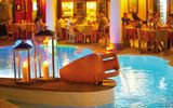 Stimmungsvoll beleuchteter Poolbereich mit Wasserspiel in Tonkrugform und dekorativen Laternen, im Hintergrund ein elegantes Restaurant mit Gästen bei Abendessen.