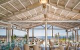 Luftiges Restaurant mit Strohdach und gemütlichen Sitzbereichen, direkt am Meer gelegen – ideal für ein entspanntes Essen mit Meerblick.