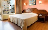 Ein einfach eingerichtetes Hotelzimmer mit einem großen Doppelbett, orangener Wand, Holzfußboden und klassischem Holzmobiliar, mit Blick aus dem Fenster auf benachbarte Gebäude.