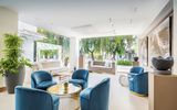 Eleganter Lounge-Bereich im Occidental Puerto Banús mit modernen blauen Samtsesseln, stilvollen Kunstwerken, großen Fenstern und Blick auf die grüne Gartenanlage.