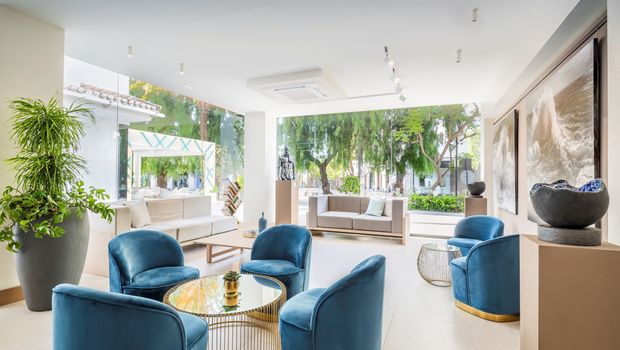 Eleganter Lounge-Bereich im Occidental Puerto Banús mit modernen blauen Samtsesseln, stilvollen Kunstwerken, großen Fenstern und Blick auf die grüne Gartenanlage.