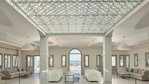 Elegante Hotel-Lobby mit kunstvoller Decke, modernen Sitzgruppen und direktem Blick auf das funkelnde Meer – stilvoller Empfang in traumhafter Umgebung.