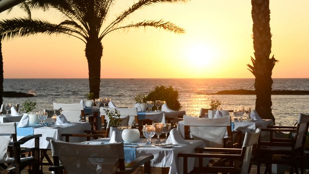 Stimmungsvoll gedeckte Tische auf der Restaurantterrasse mit Blick auf das Meer und einen traumhaften Sonnenuntergang.
