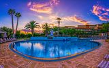 Großer Hotelpool mit Palmenkulisse bei Sonnenuntergang – das Wasser spiegelt den farbenprächtigen Himmel, umrahmt von Liegestühlen und mediterranem Ambiente.