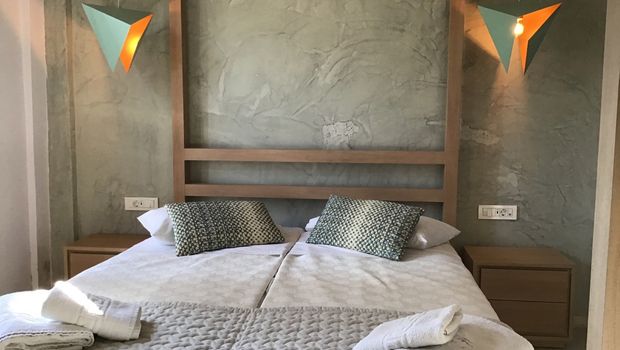 Modern eingerichtetes Doppelzimmer mit zwei zusammengestellten Einzelbetten, dekorativen Kissen und auffälligen Designer-Hängelampen – warme Holz- und Naturtöne sorgen für eine gemütliche Atmosphäre.