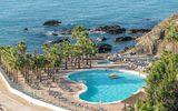 Großzügige Poolanlage direkt an der felsigen Küste mit zahlreichen Palmen, Liegestühlen und einem separaten Whirlpool – perfekter Ort zum Entspannen mit Blick aufs Meer.