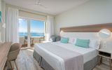 Helles, modern eingerichtetes Hotelzimmer mit Doppelbett, Schreibtisch und Zugang zu einem Balkon mit traumhaftem Meerblick.