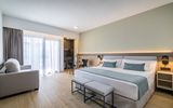Modernes, geräumiges Hotelzimmer mit Kingsize-Bett, hellen Holzböden, gemütlicher Sitzecke, Schreibtisch und bodentiefen Fenstern, die viel Tageslicht hereinlassen.