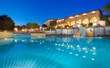 Stimmungsvoll beleuchteter Hotelpool in der Dämmerung mit Wasserrutsche, gemütlichen Liegeinseln und elegantem Hotelgebäude im Hintergrund – ideal für entspannte Abende in mediterranem Ambiente.