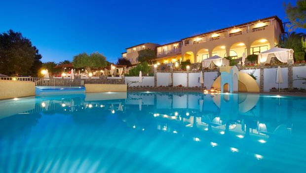 Stimmungsvoll beleuchteter Hotelpool in der Dämmerung mit Wasserrutsche, gemütlichen Liegeinseln und elegantem Hotelgebäude im Hintergrund – ideal für entspannte Abende in mediterranem Ambiente.