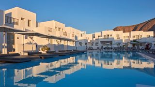 Modernes Hotel im kubischen Stil mit weiß getünchten Fassaden, großzügigem Poolbereich und bequemen Liegen unter Sonnenschirmen – ideal zum Entspannen in der Abendsonne.