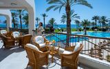 Terrasse mit gemütlichen Rattanmöbeln und Meerblick – im Hintergrund der Poolbereich, Palmen und das glitzernde Mittelmeer.