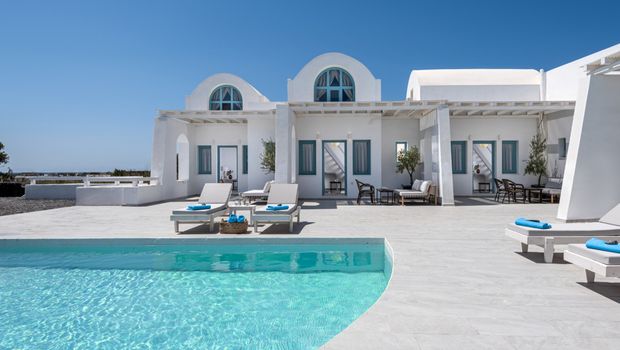 Modernes Boutique-Hotel im kykladischen Stil mit weißer Fassade, blauen Fensterläden und Poolterrasse mit Liegen – klare Architektur und mediterranes Flair unter strahlend blauem Himmel.