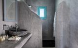 Modernes Badezimmer mit glatten Betonwänden, offenem Duschbereich und stilvollem Naturstein-Waschbecken – minimalistische Gestaltung mit hochwertigen Materialien.
