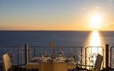 Romantisch gedeckter Tisch für zwei mit Meerblick bei Sonnenuntergang – Weingläser, Besteck und warme Lichtstimmung.